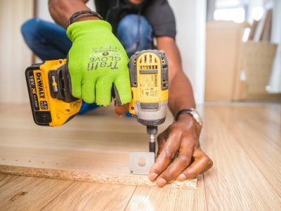 Man using a power drill for home improvement on a wooden floor with precision.